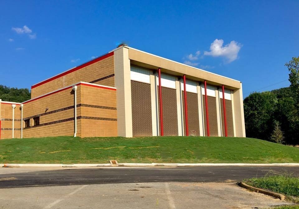 A large brick building with red and white stripes is sitting on top of a grassy hill.