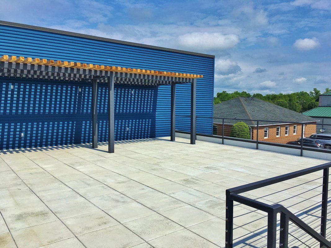 A rooftop deck with a pergola and a blue building in the background.