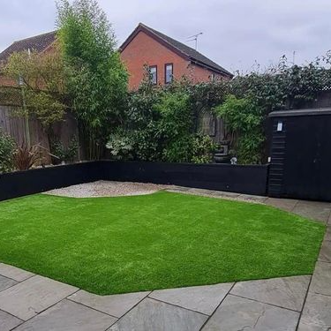 A backyard with a lush green artificial grass  lawn and a black fence.