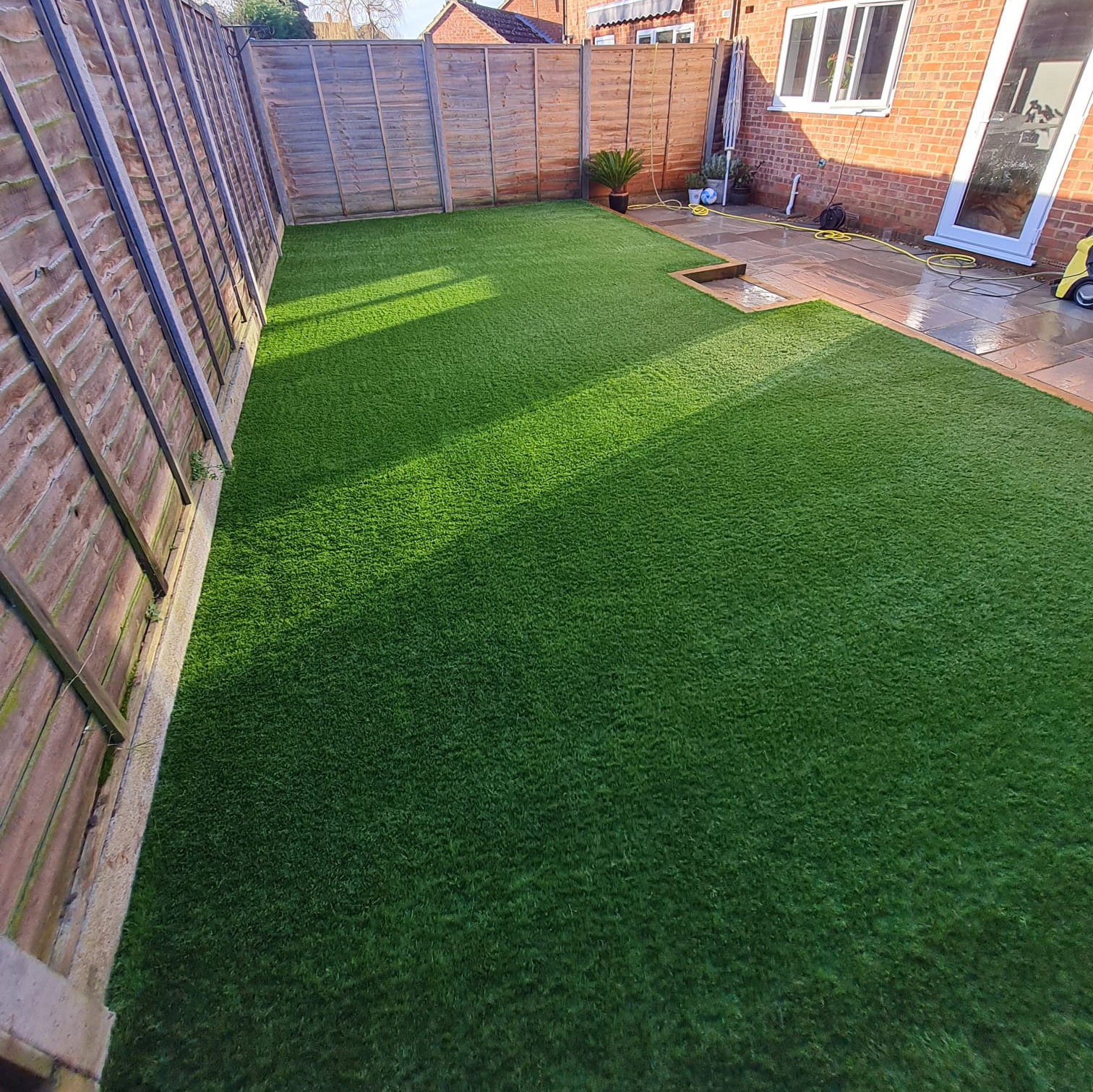 A backyard with a wooden fence and a lush green artificial grass lawn.