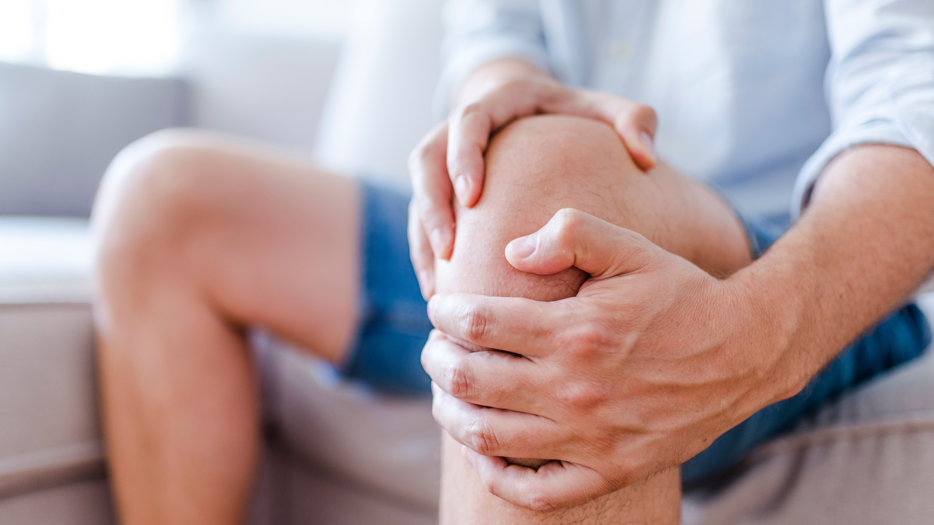 Person seated, holding knee, indicating pain. Indoors, daylight.
