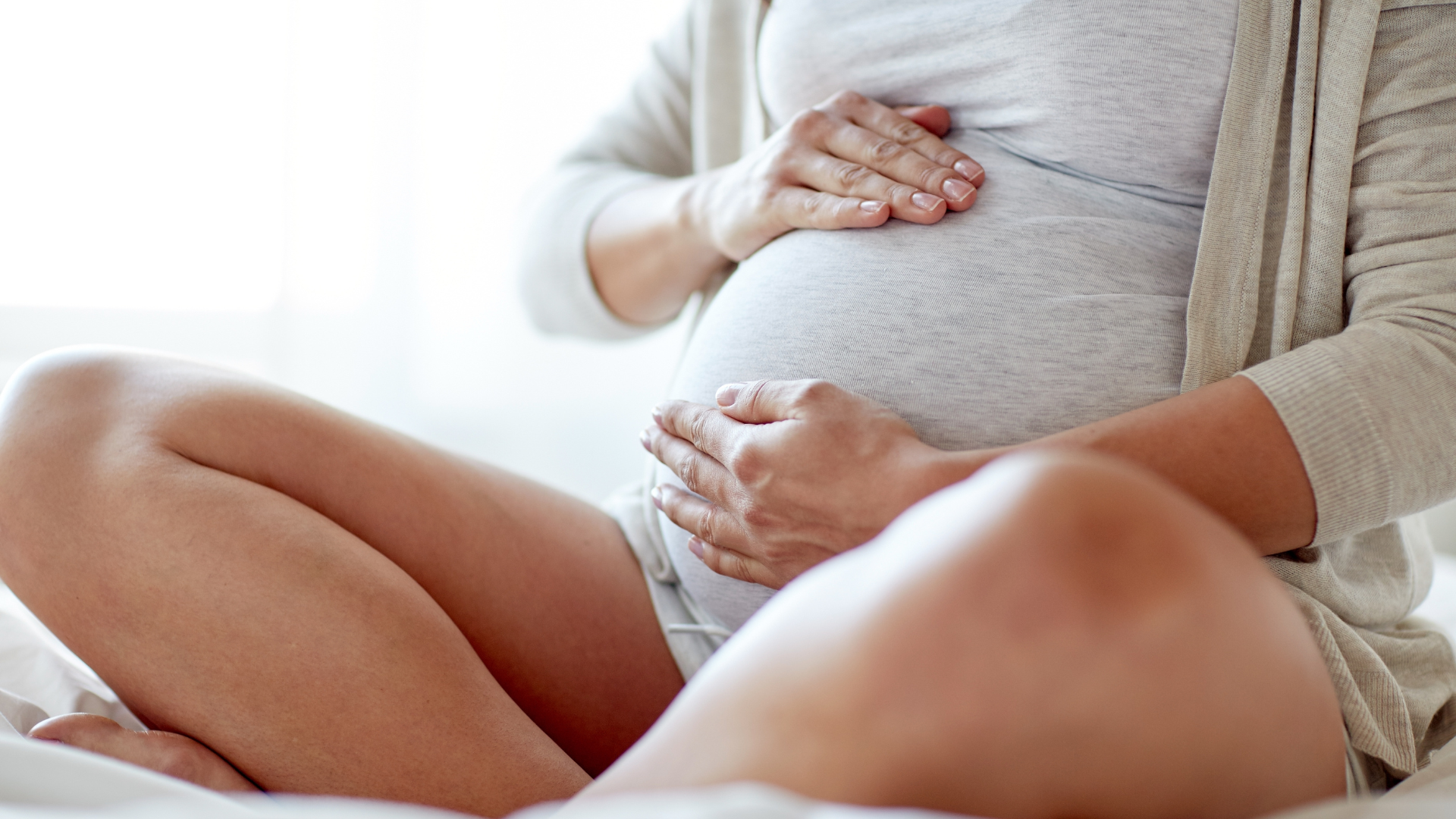 Pregnant person seated, hands on belly, soft lighting.