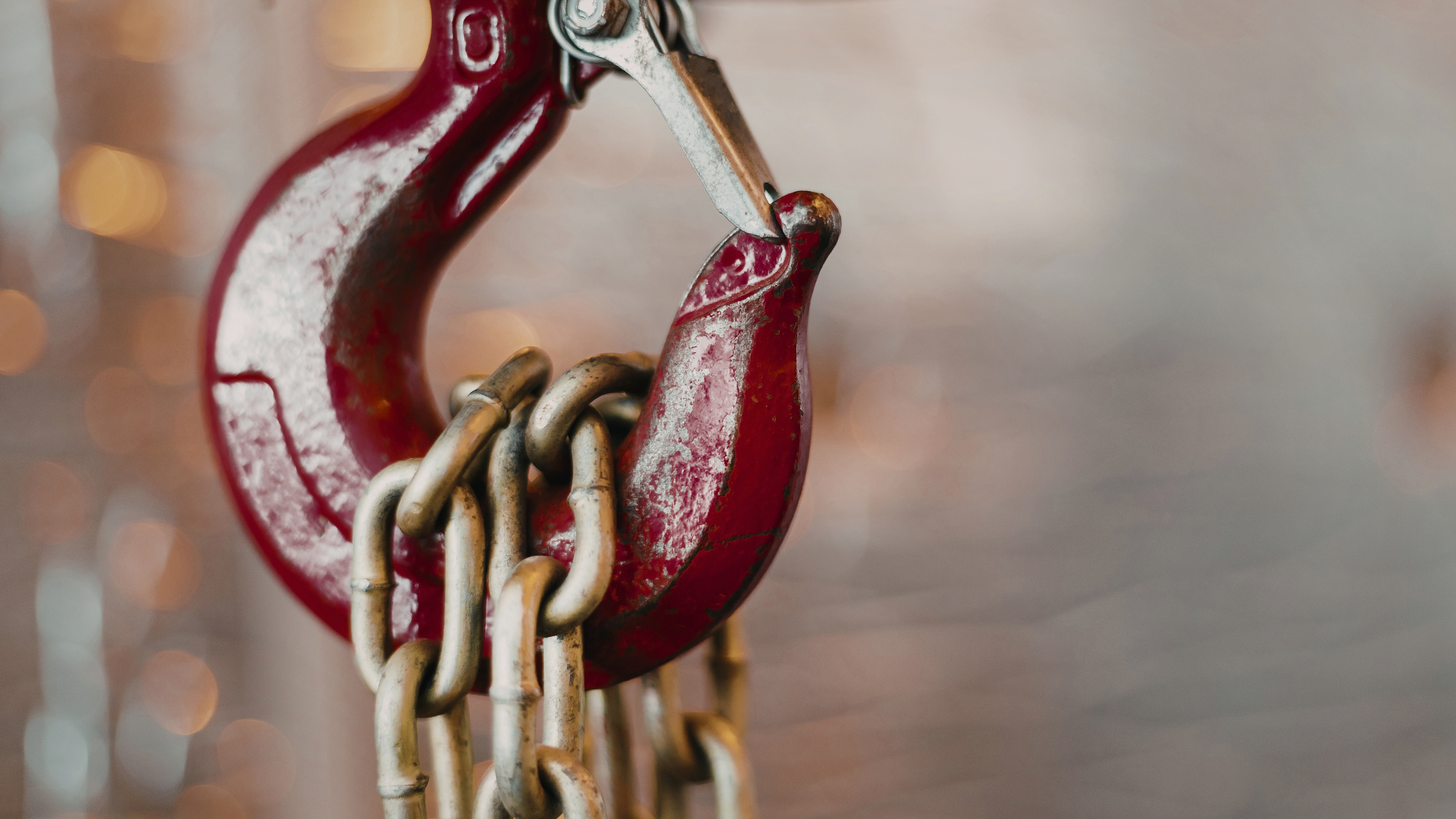 Red metal chain hook with interlinked chains against a blurred background