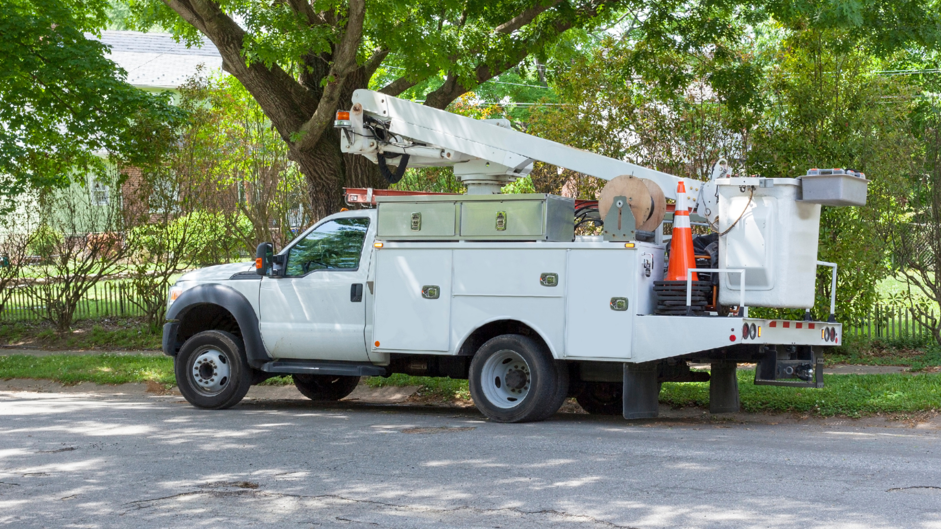 White utility truck with an extended bucket lift parked under trees on a roadside