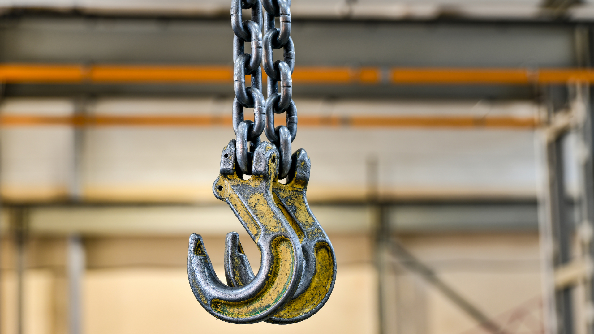 Close-up of a metal chain hoist with yellow hooks hanging in an industrial warehouse.