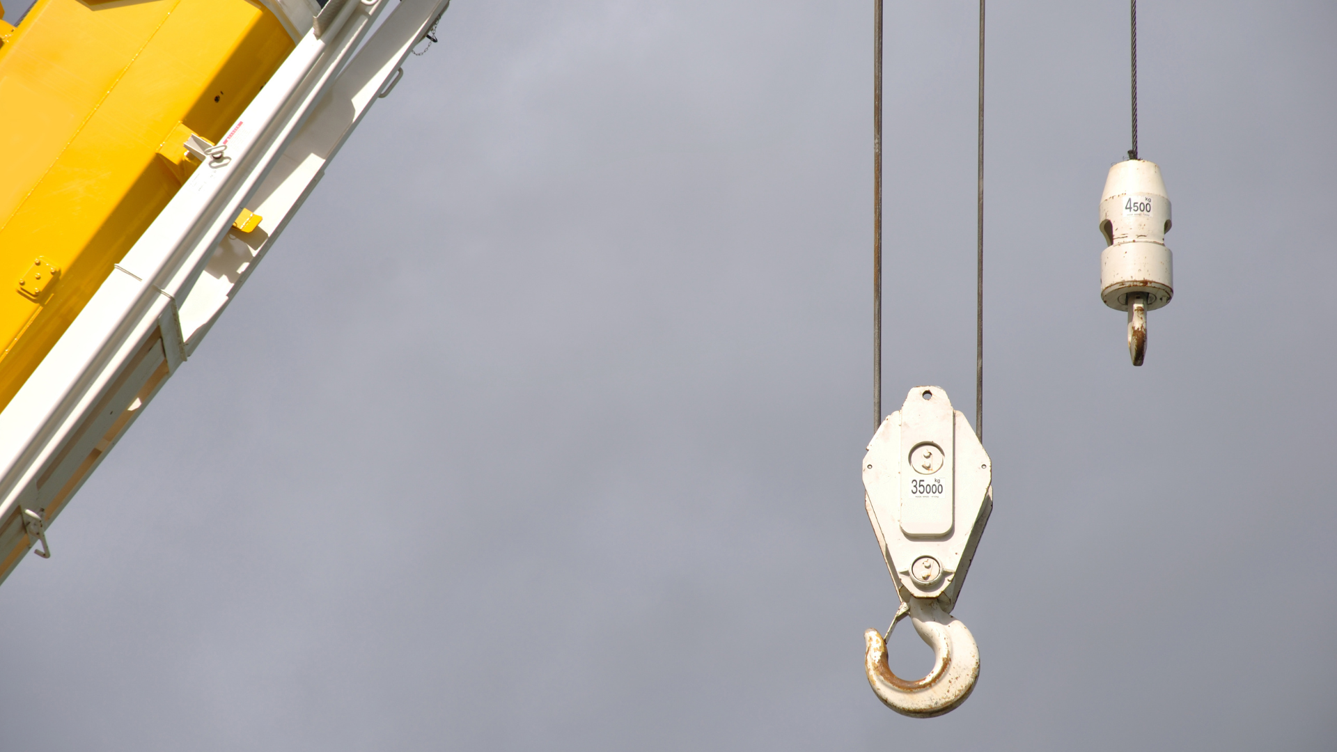 Yellow crane boom with hanging hook and pulley against a cloudy sky