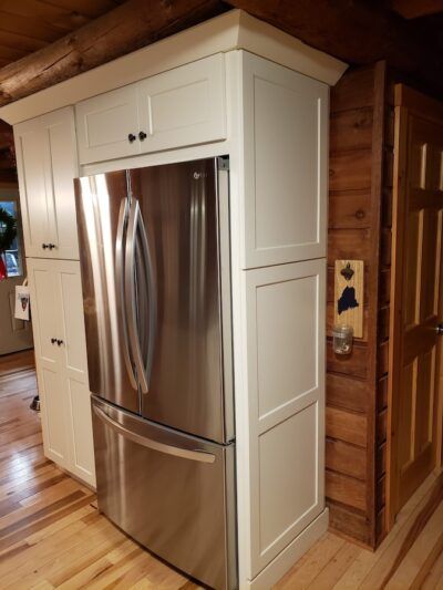 Stainless steel refrigerator built into white cabinets in a rustic kitchen with wood floors.