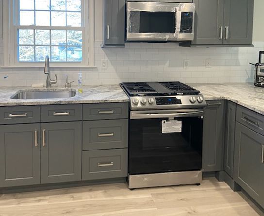 Gray kitchen cabinets and appliances, stainless steel range, light countertops, and window.