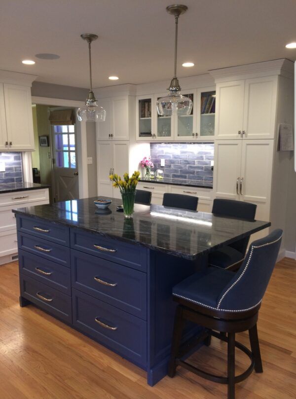 Blue kitchen island with dark countertop and two pendant lights. White cabinets and wood floors.