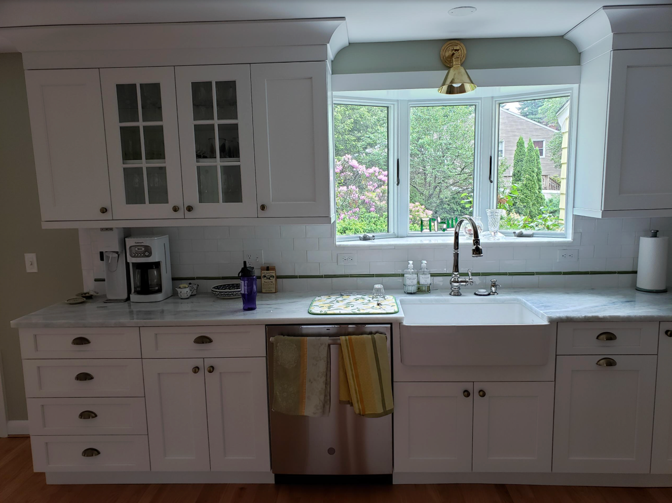 White kitchen cabinets with a farmhouse sink under a window overlooking a green yard.