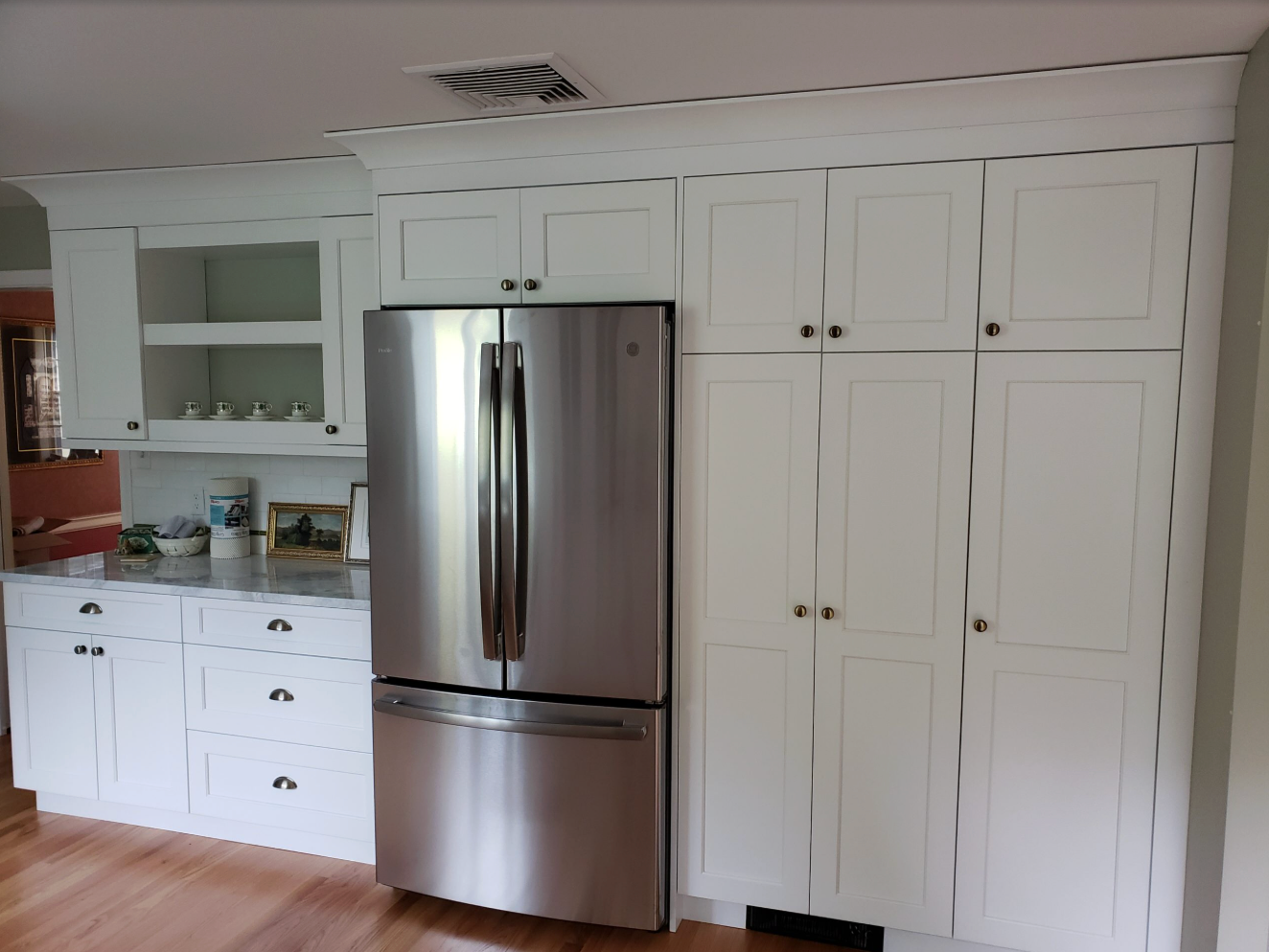 White kitchen cabinets and stainless steel refrigerator against a wall.