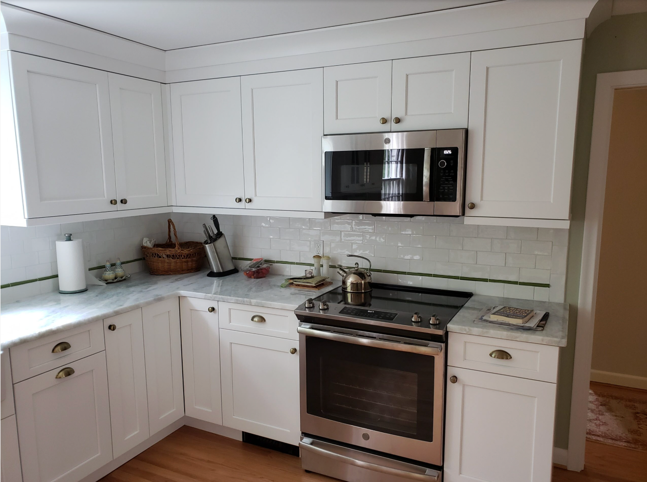 White kitchen cabinets with a stainless steel oven and microwave; marble countertops.