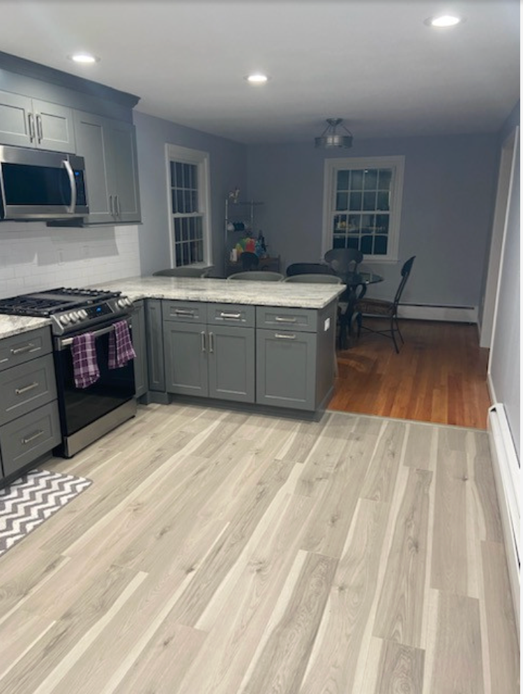 Gray kitchen with island, stainless steel appliances, and wood-look flooring. Dining area with table and chairs.