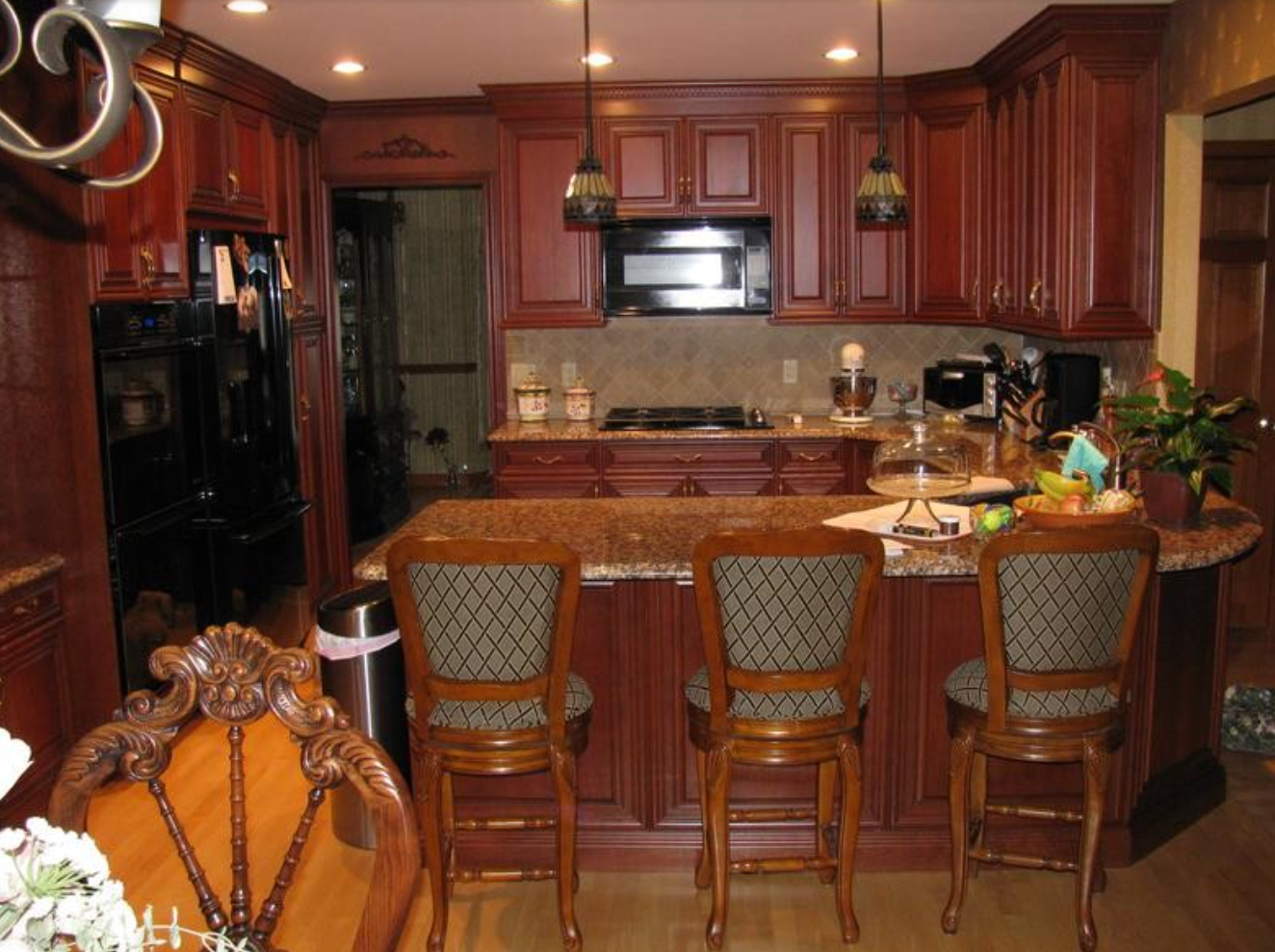 Kitchen with brown cabinets, island with stools, and black appliances.