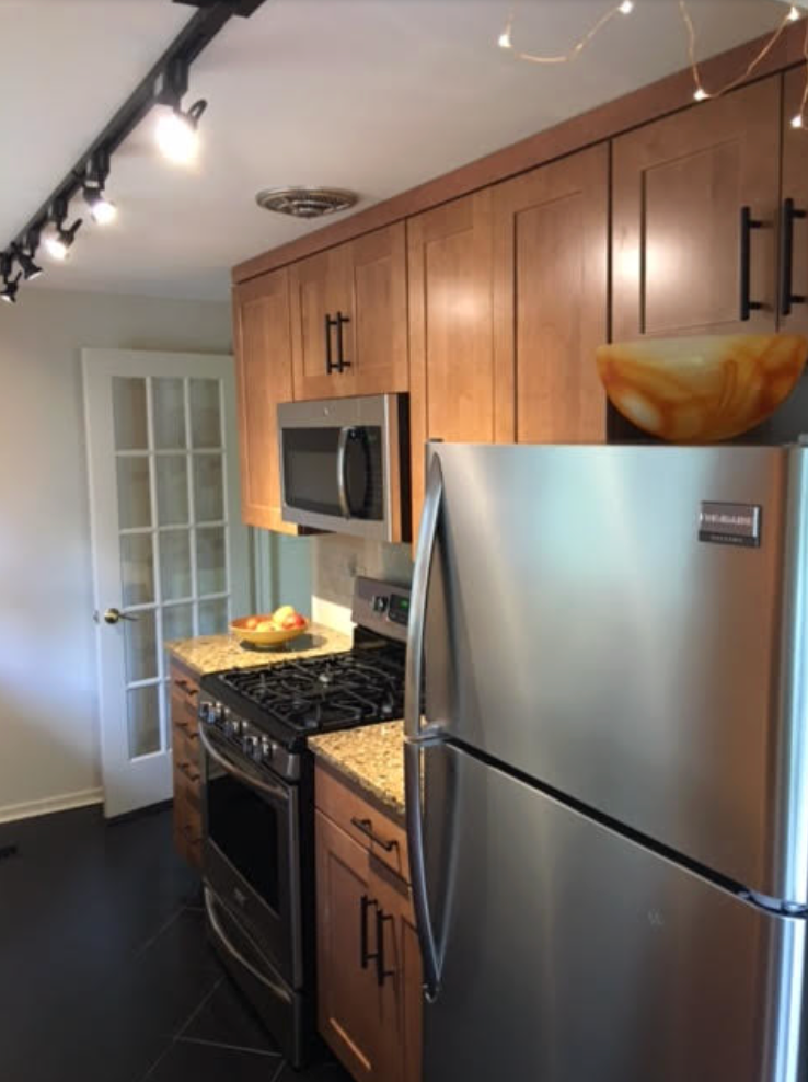 Kitchen with stainless steel appliances, wood cabinets, and black floor tiles.
