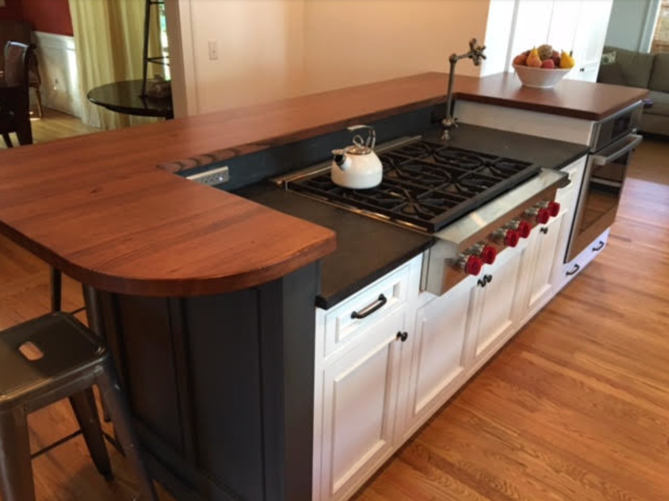 Kitchen island with gas stove, wooden countertop, white cabinets, and a bar area.