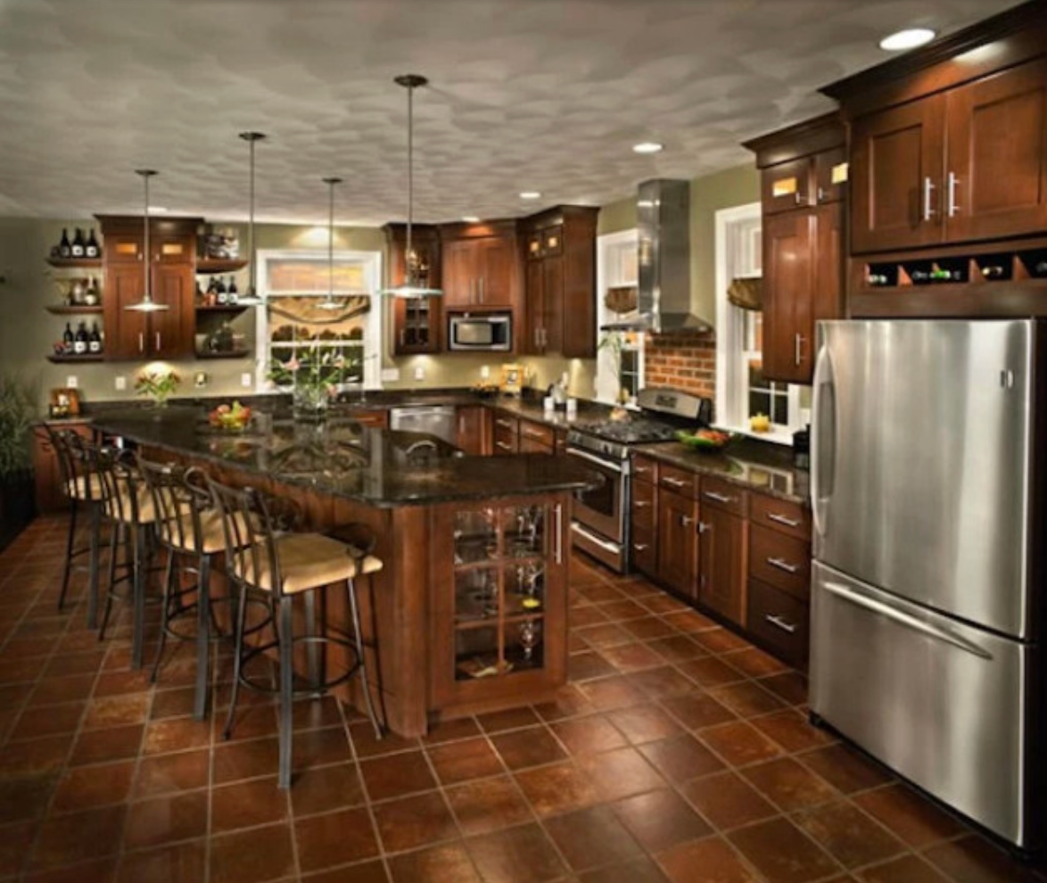 Spacious kitchen with dark wood cabinets, island with bar stools, stainless steel appliances, and terracotta tile floors.