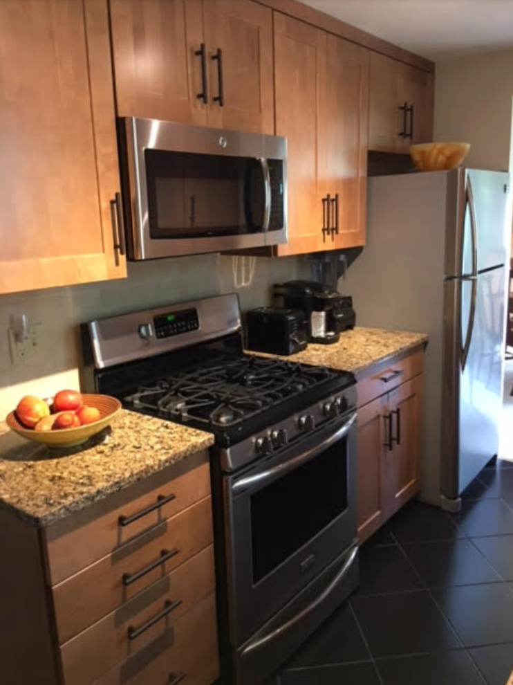 Kitchen with stainless steel appliances, wood cabinets, granite countertops, and a bowl of fruit.