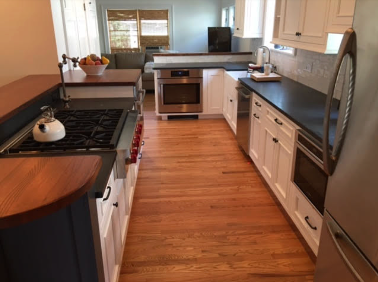 A galley kitchen with white cabinets, wood countertops, and stainless steel appliances.