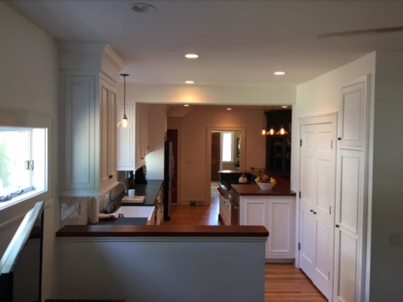 Bright kitchen with white cabinets, wood countertops, and an open doorway to another room.