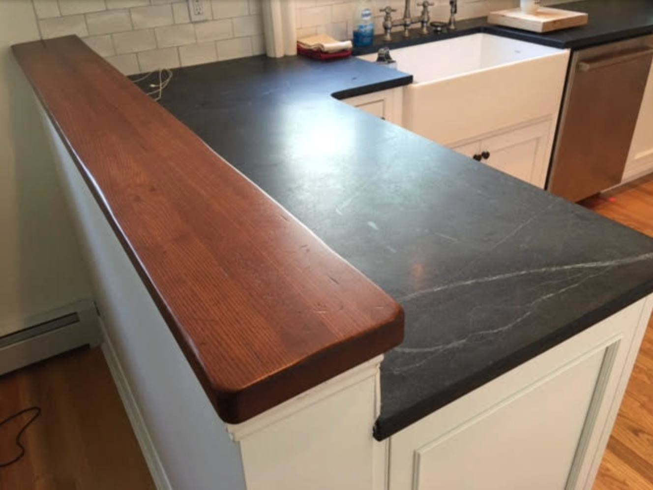 Kitchen countertop with dark gray stone, white cabinets, and a wood bar.