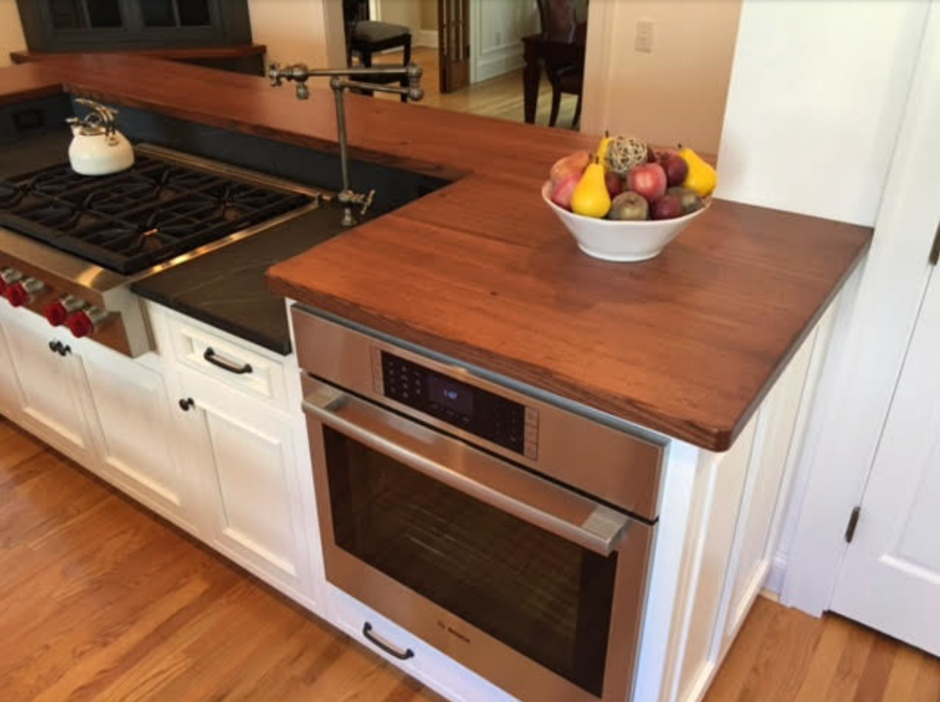 Kitchen with wood countertops, oven, stove, white cabinets, and bowl of fruit.