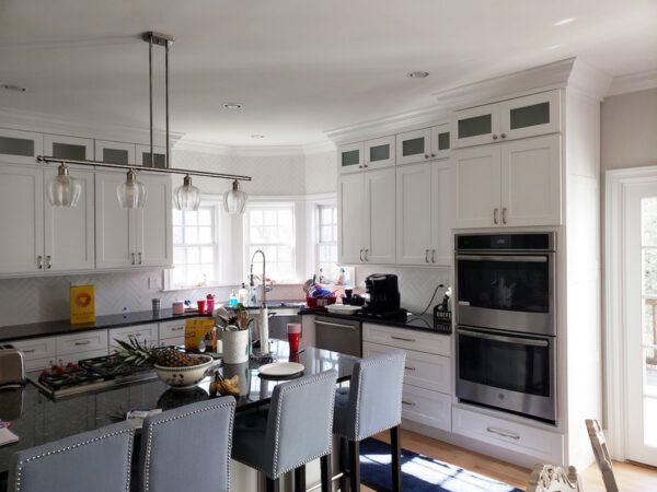 White kitchen with black countertops, island with stools, and stainless steel appliances.