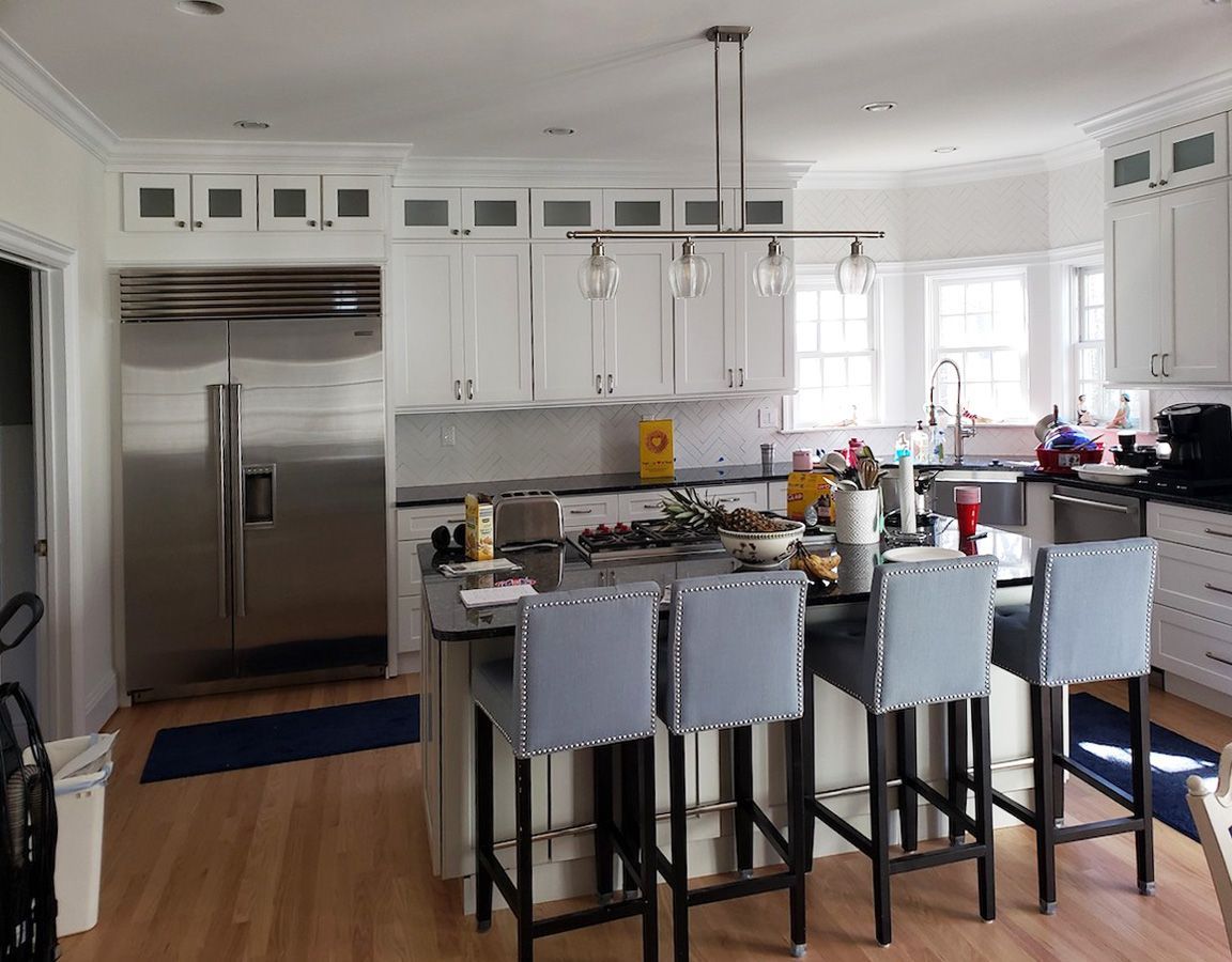 White kitchen with island and stainless steel refrigerator, island stools, and overhead lighting.