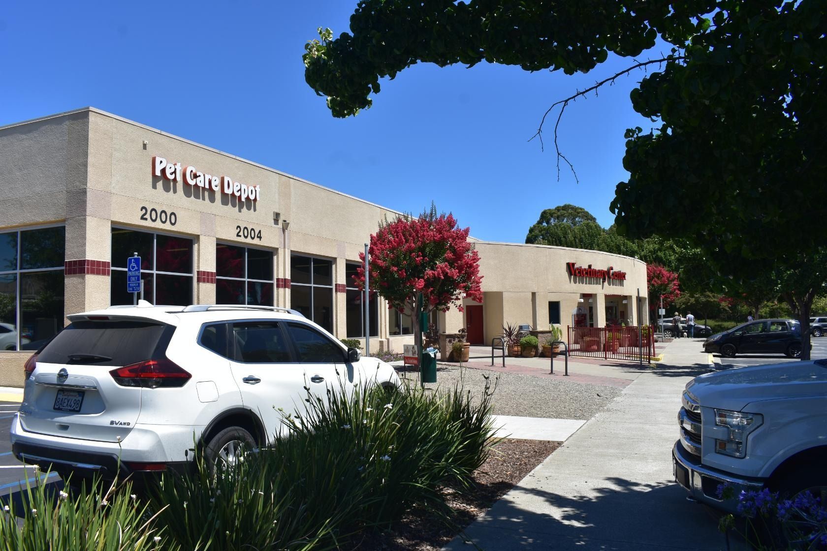 Exterior of a strip mall with a white SUV, a bakery, and a pet store on a sunny day.
