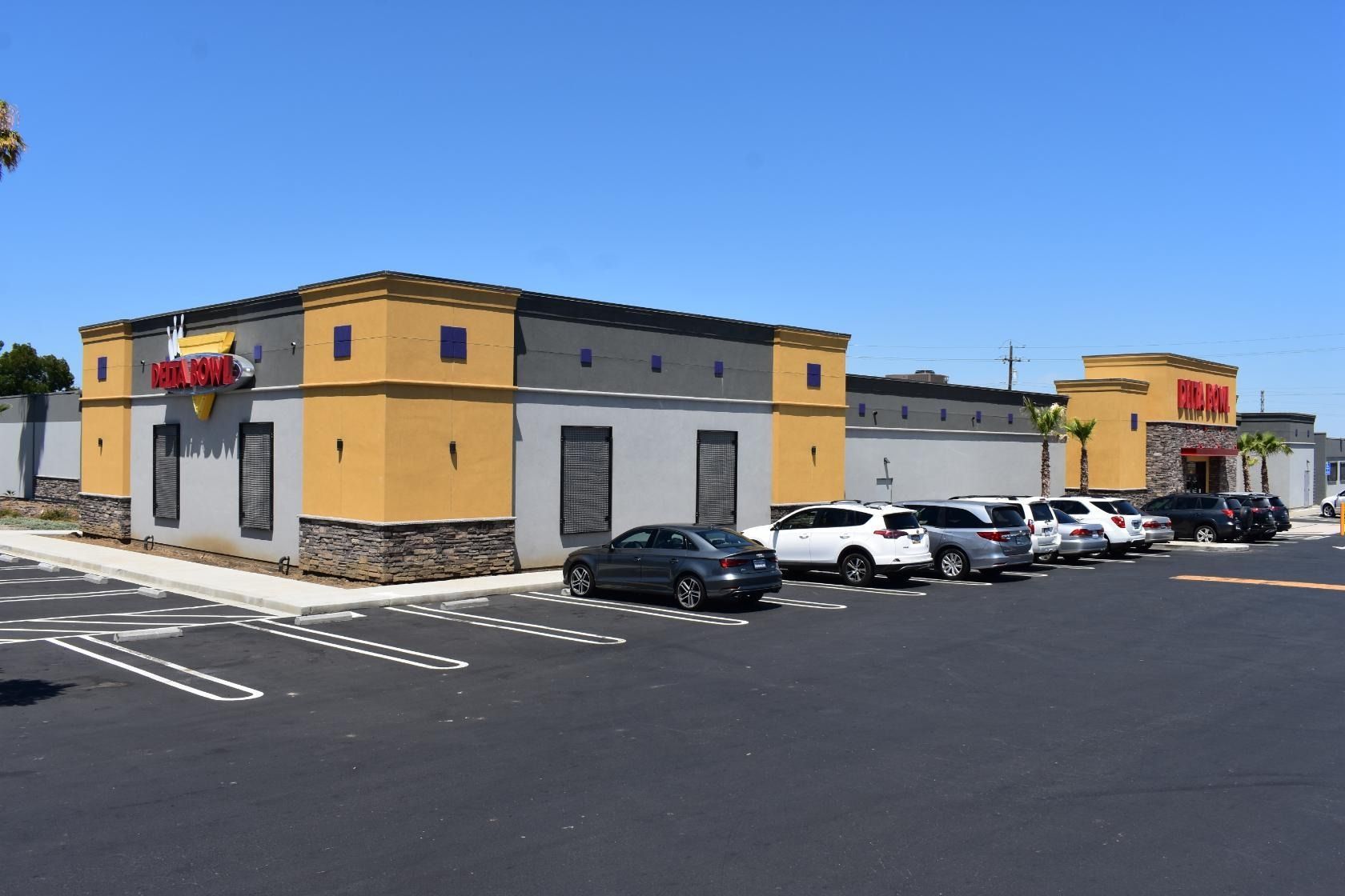 Restaurant building with tan and gray exterior, cars parked in front, under a clear blue sky.