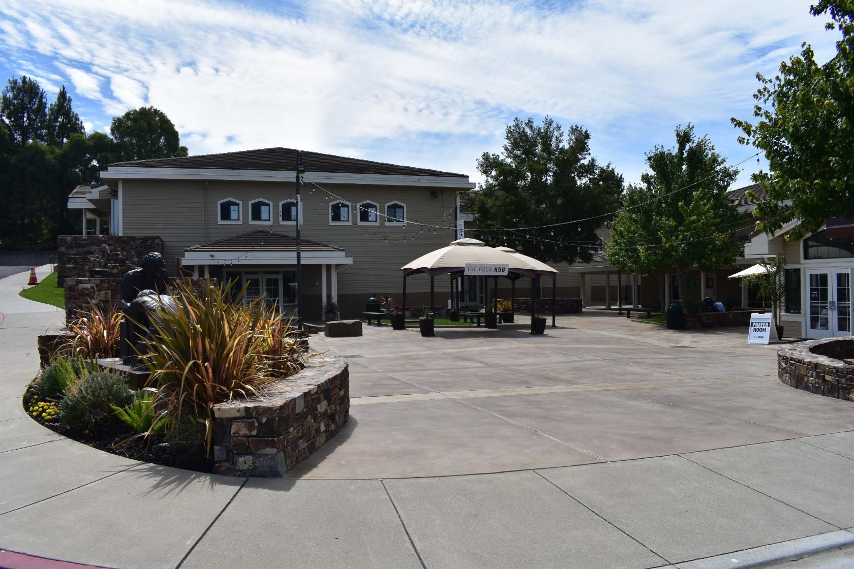 Outdoor patio with a tan building, trees, and a covered seating area.