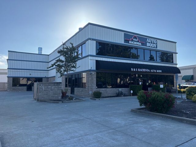 Exterior of "Basima Auto Body" building with large windows and awning, set against a blue sky.