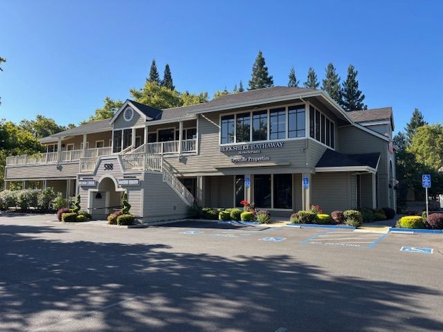 Two-story, gray-sided commercial building with multiple windows, shrubs, and a few handicap parking spaces.