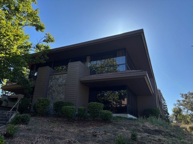 Brown mid-century modern house with angled roof, large windows, on a hillside. Blue sky.