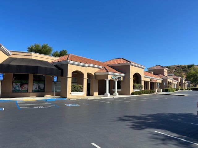 Exterior view of a beige commercial building with a tiled roof and empty parking lot under a clear blue sky.