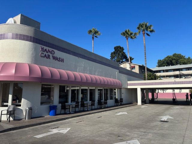 Exterior of a hand car wash with pink accents, palm trees, and blue sky.