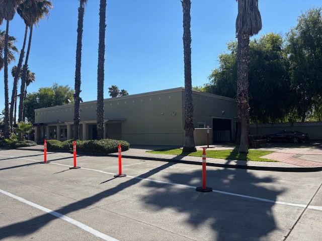Building with palm trees in front, orange cones, and blue sky.