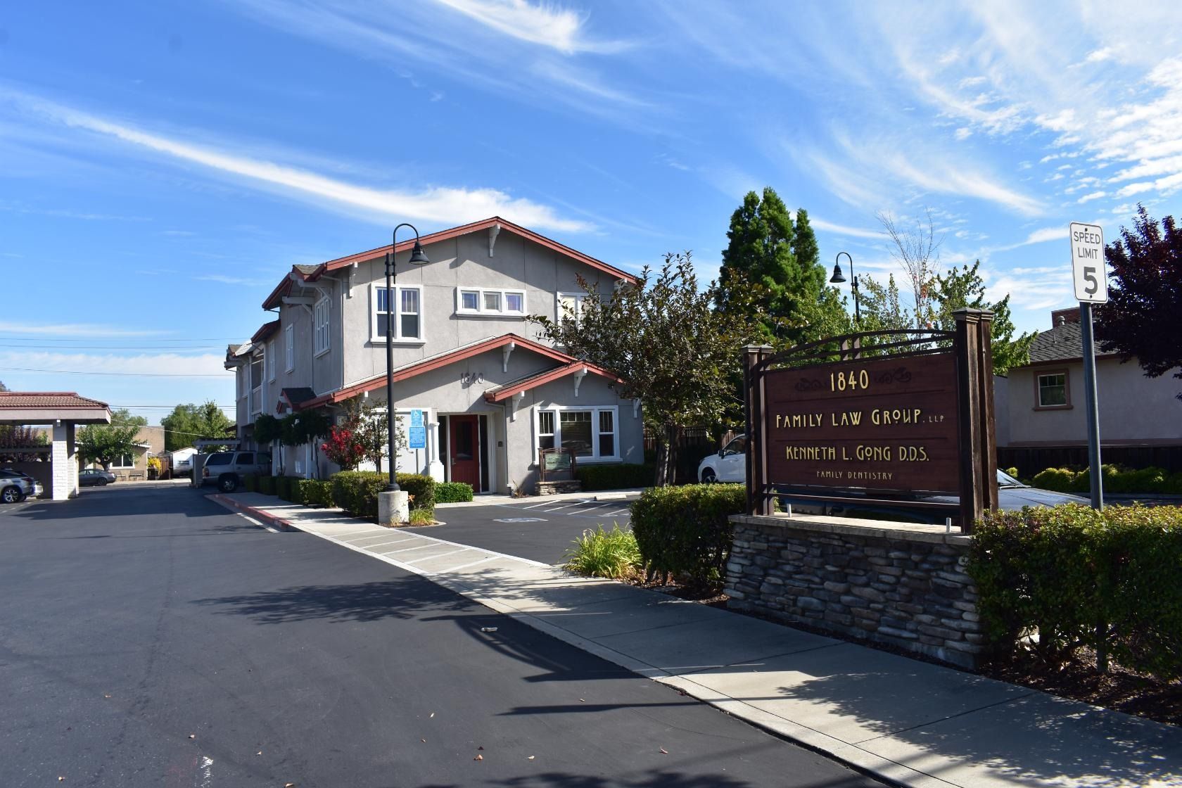 Two-story light gray building with red-tiled roof, sign on a brick base, under blue sky.