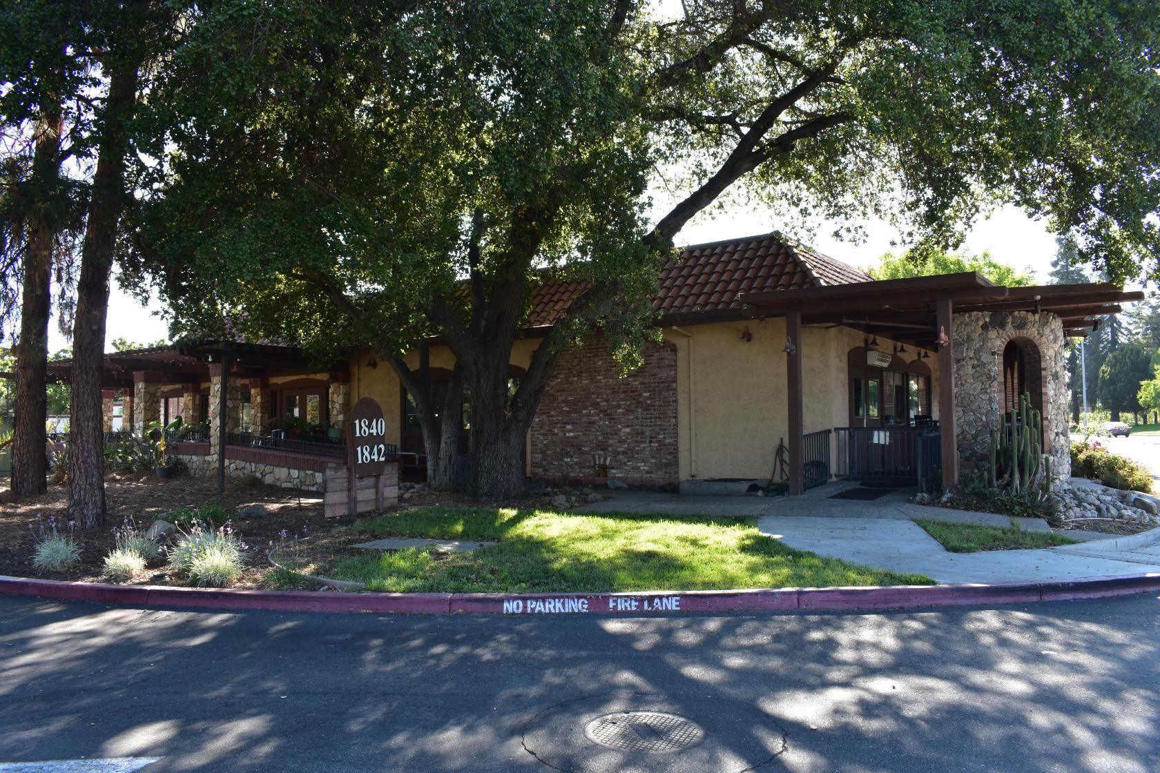 A one-story tan building with a red tile roof, stone facade, and trees in front.