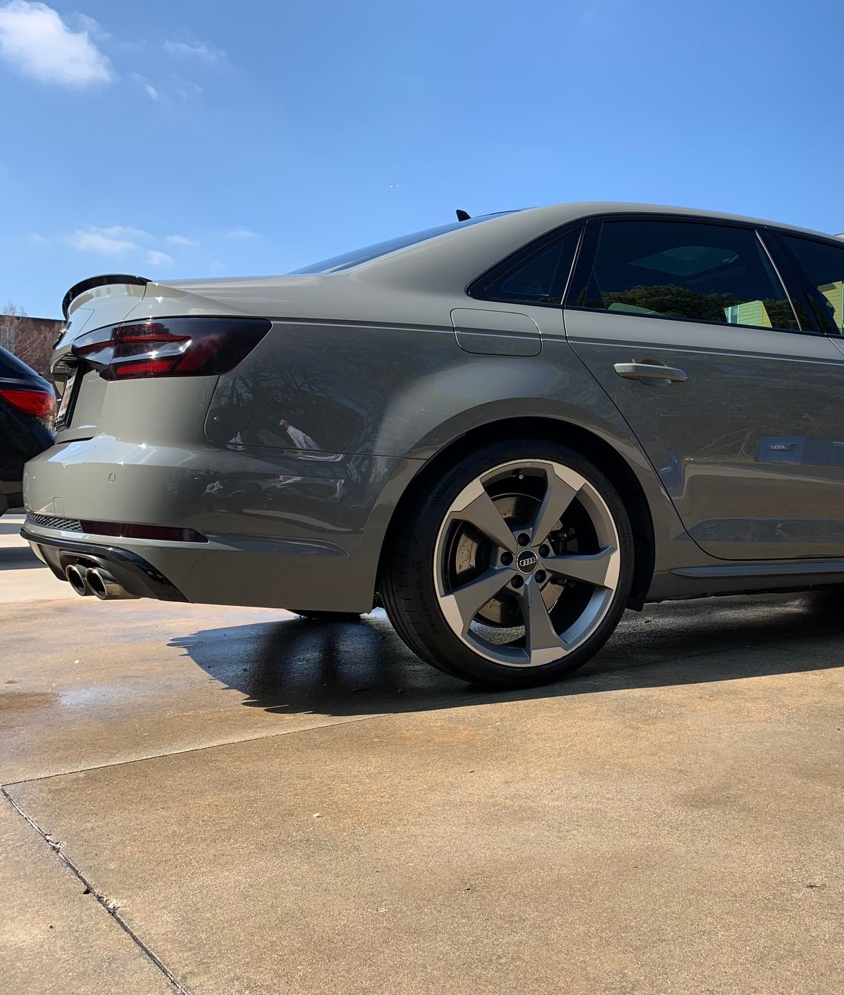 Gray Audi sedan with black spoiler and dark gray wheels, parked on a concrete surface.