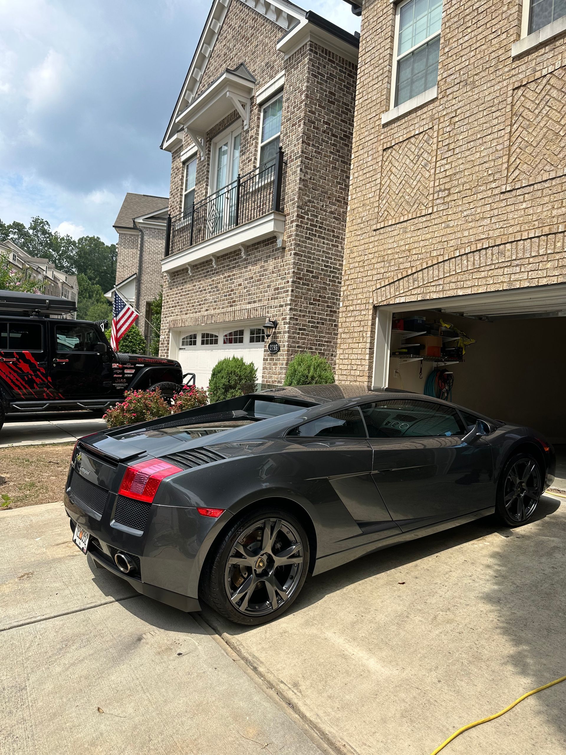 Gray Lamborghini convertible parked in front of a brick house with an open garage.