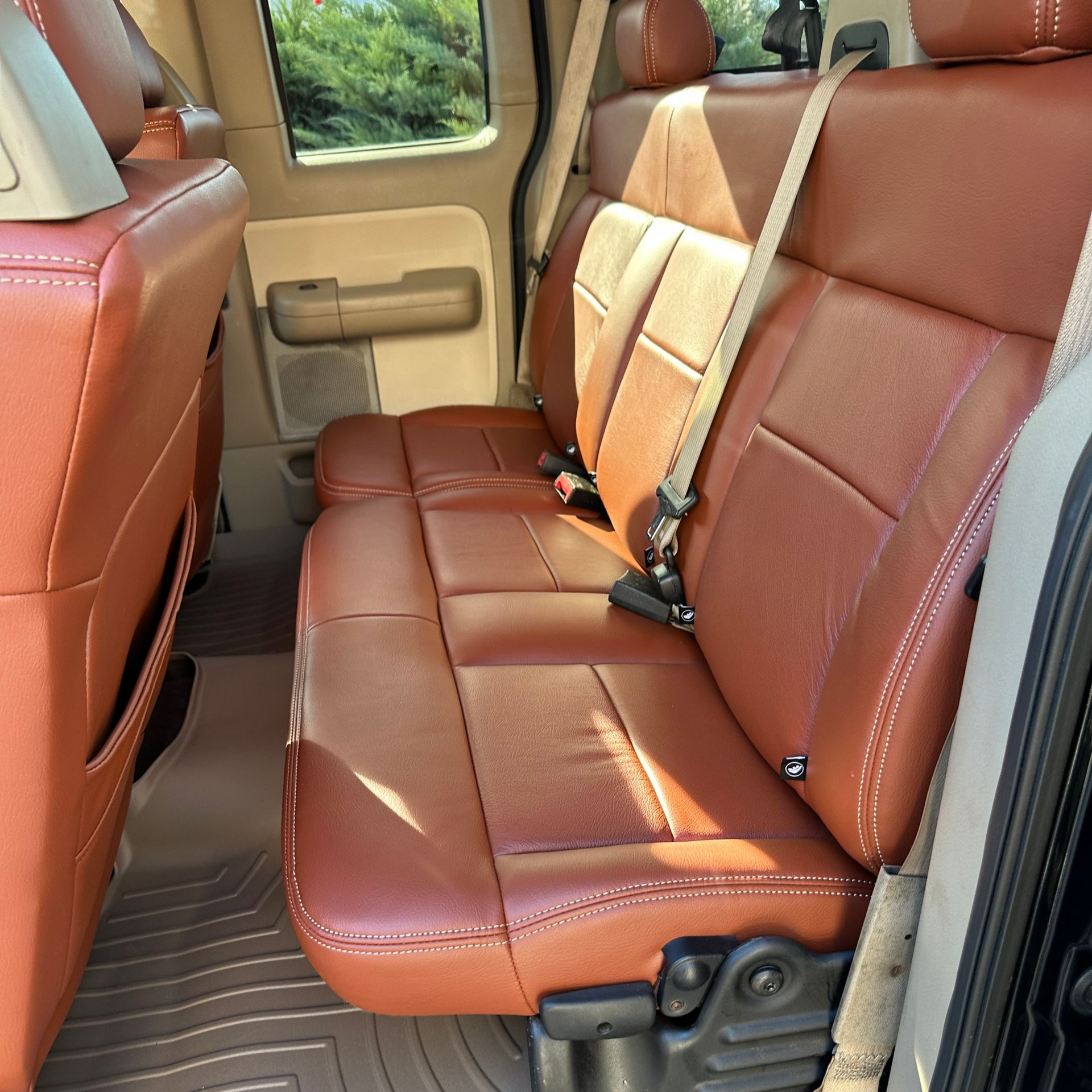 Brown leather truck backseat with tan stitching and beige floor mats.
