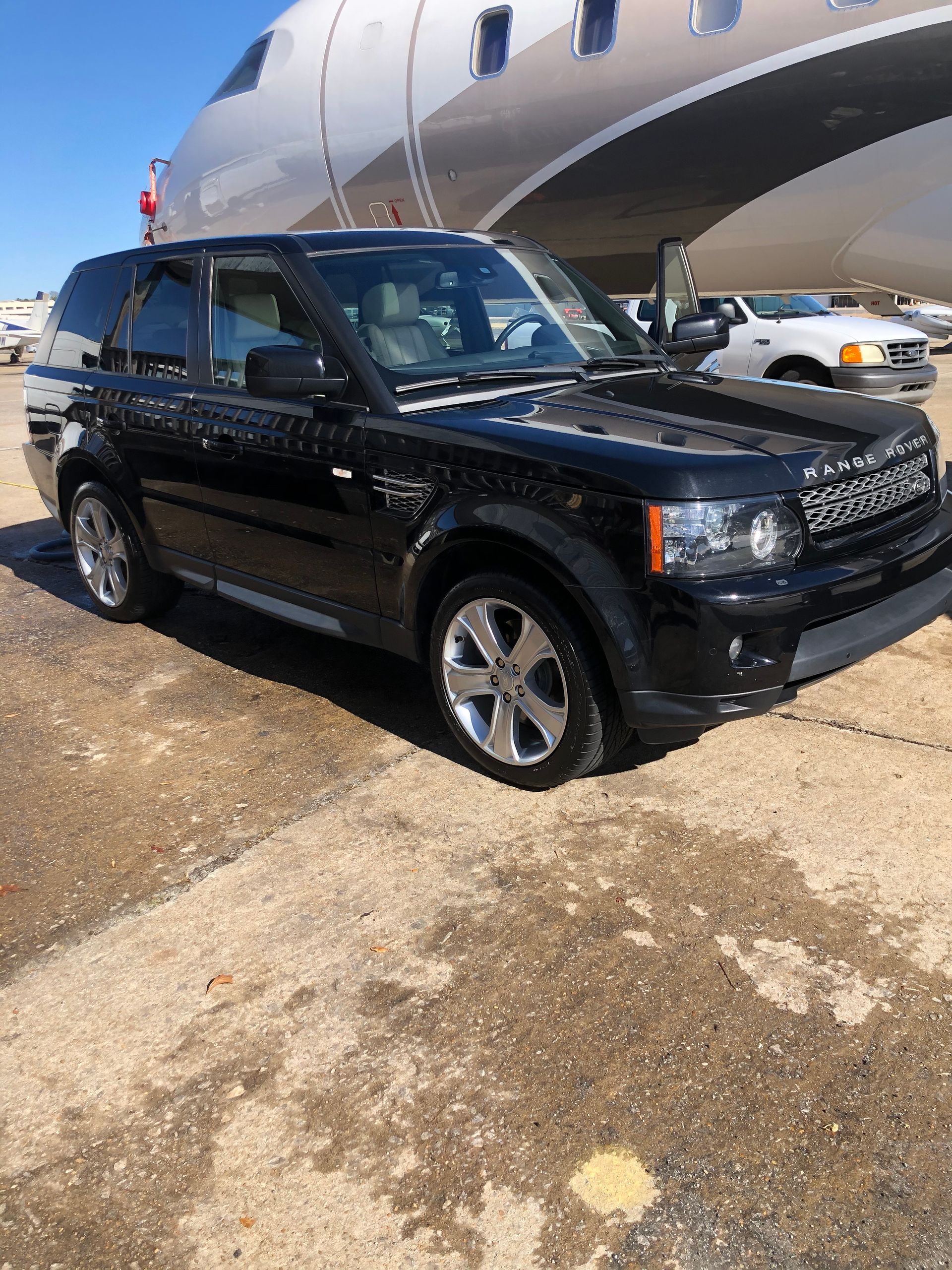 Black Range Rover SUV parked on a tarmac in front of a private jet.