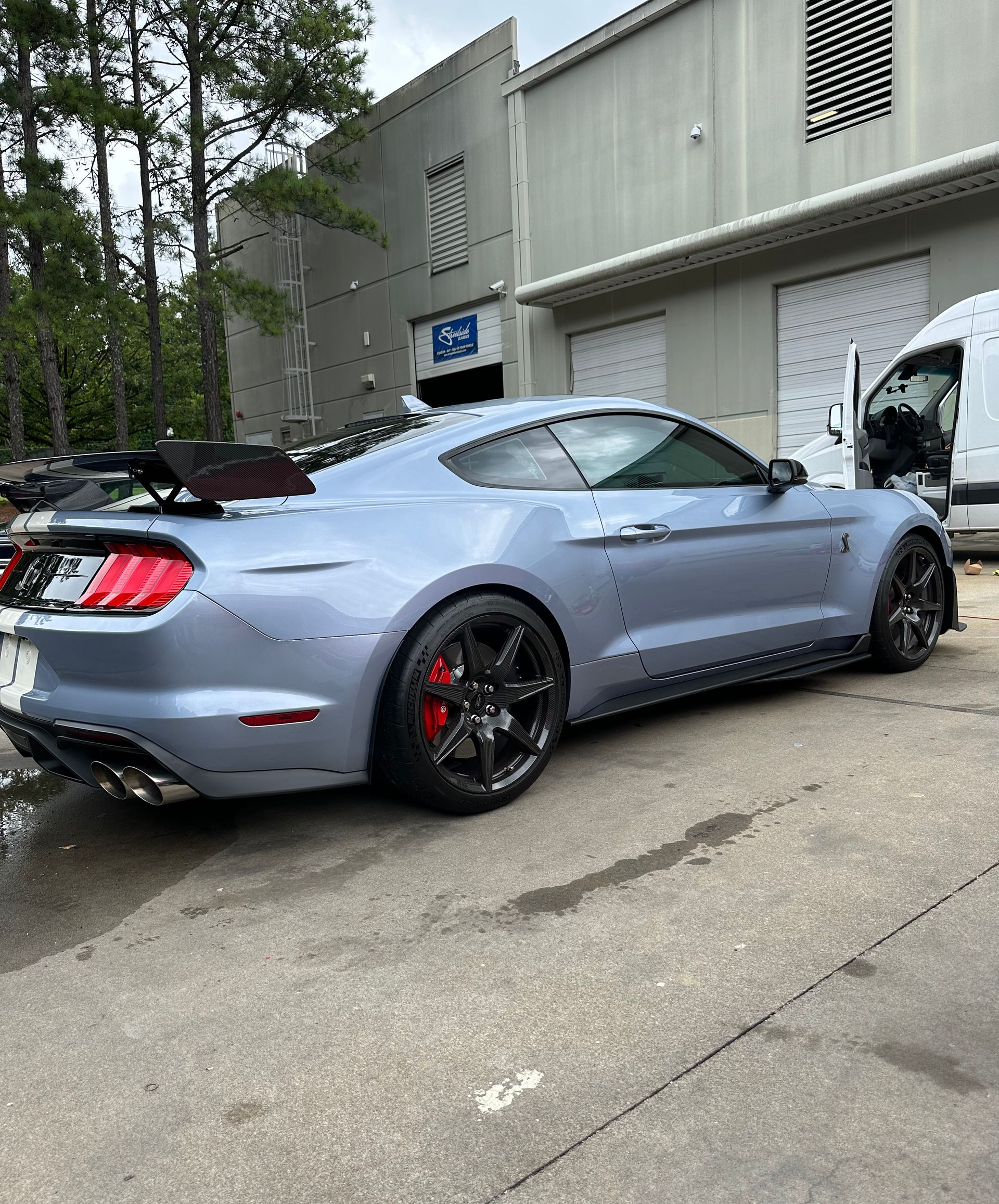 Blue sports car with black wheels parked outside a gray building. Red brake calipers visible.