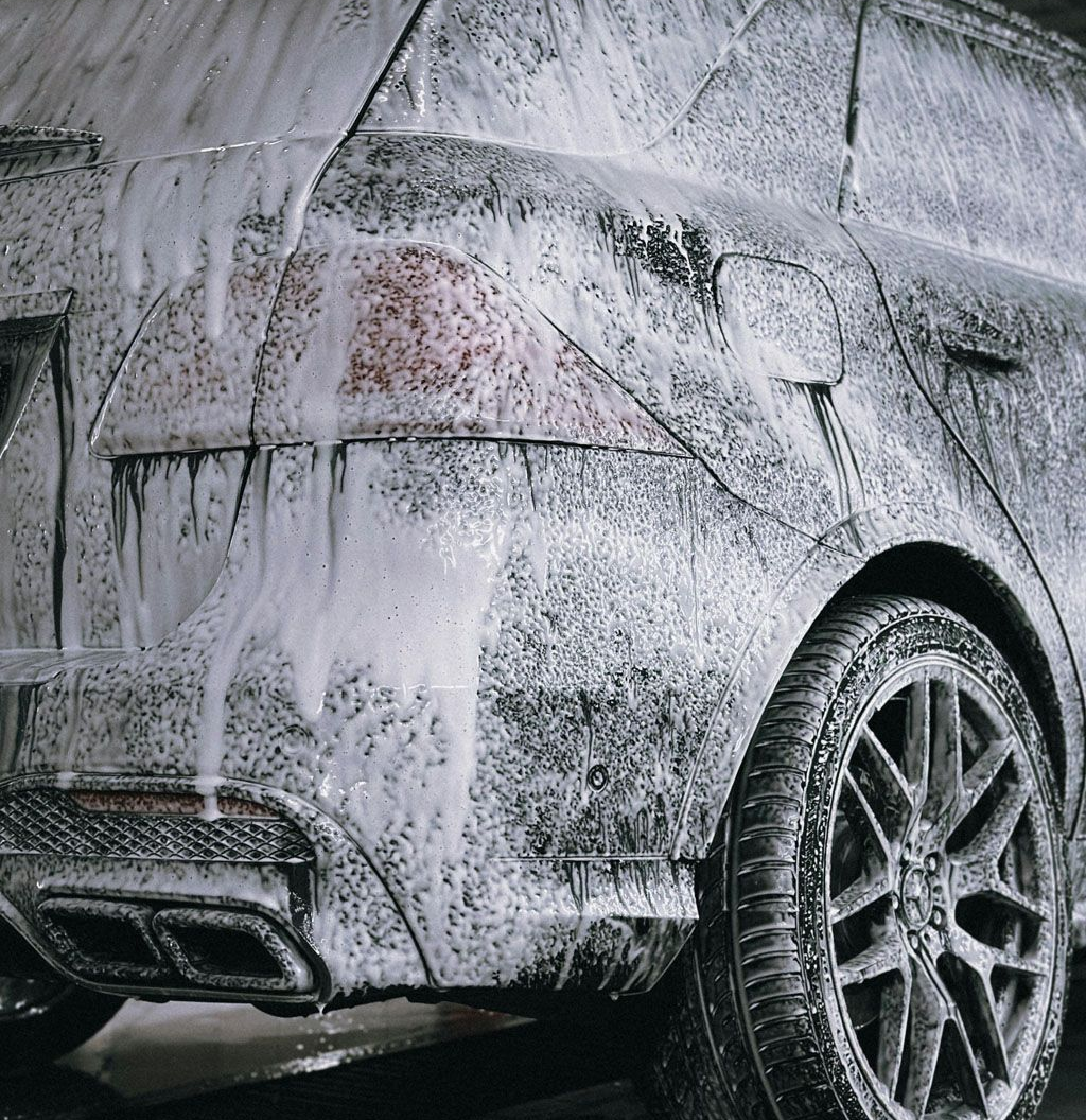 Car being washed, covered in white foam suds at a car wash.