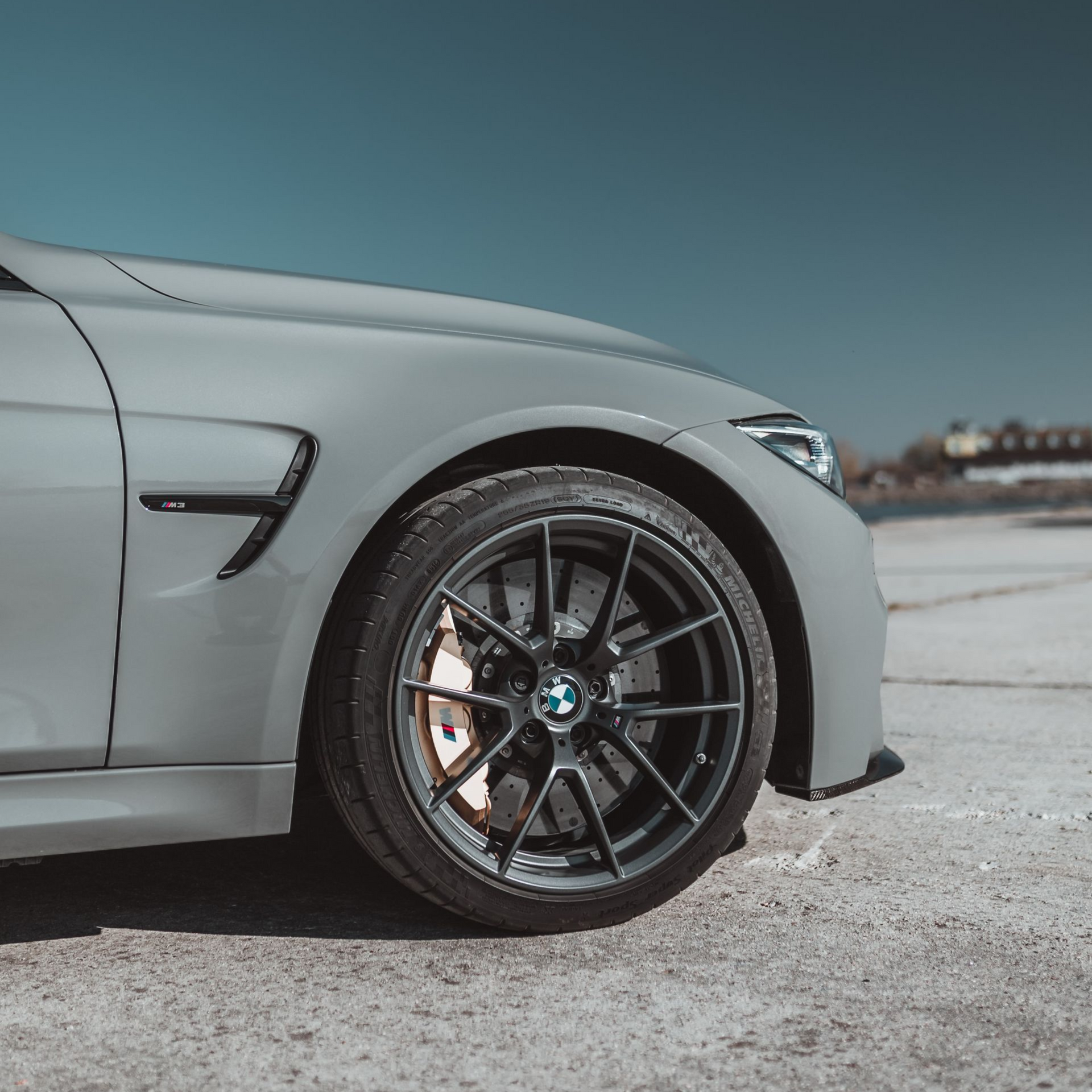 Gray BMW M4 sports car, black wheels, against a blue sky.