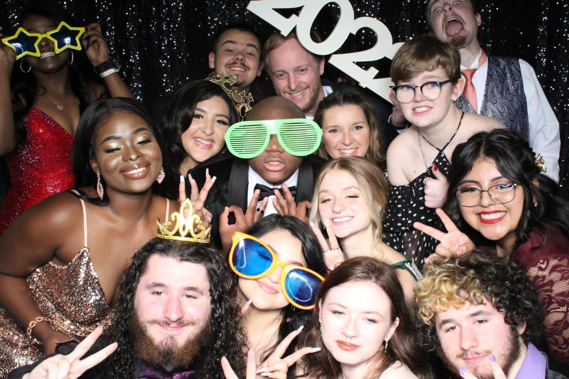 Crowded group posing at a party, wearing oversized novelty glasses and festive accessories, smiling at the camera