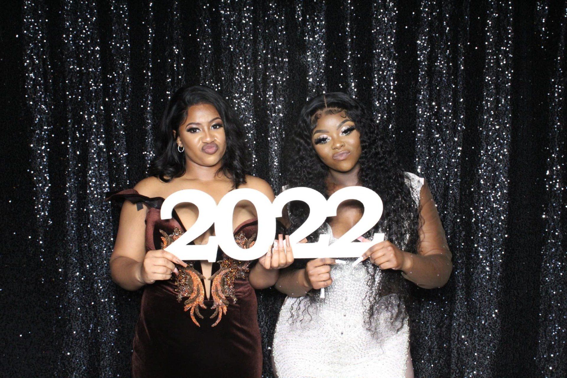 Two people holding “2022” cutout signs in front of a black sequin backdrop