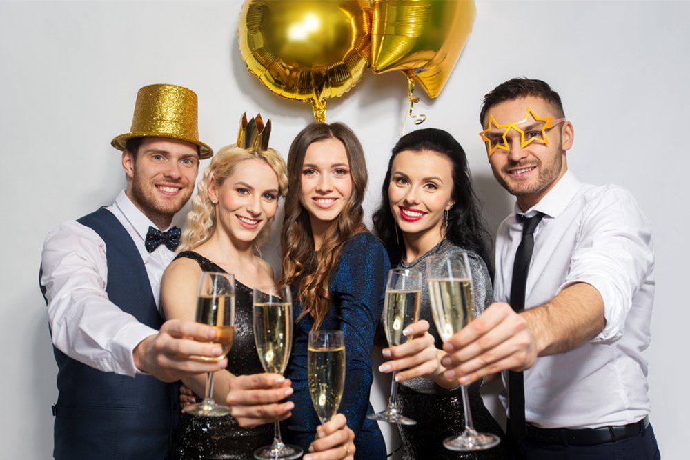 Five friends toasting champagne at a festive party with gold balloons and celebratory hats