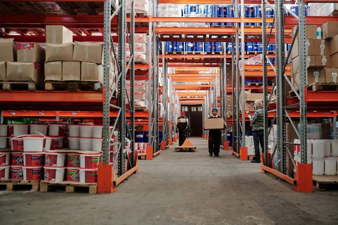 Warehouse interior with loaded shelves and workers moving boxes.